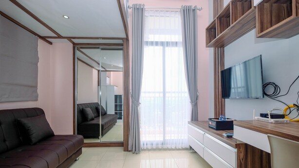 Una sala de estar moderna con un sofá marrón, un escritorio de madera, un televisor de pantalla plana y un ventanal corredero que da a un balcón.