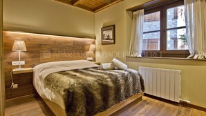 Un dormitorio con cabecera de madera, cama con manta mullida, mesita de noche con lámpara y ventana con cortinas.