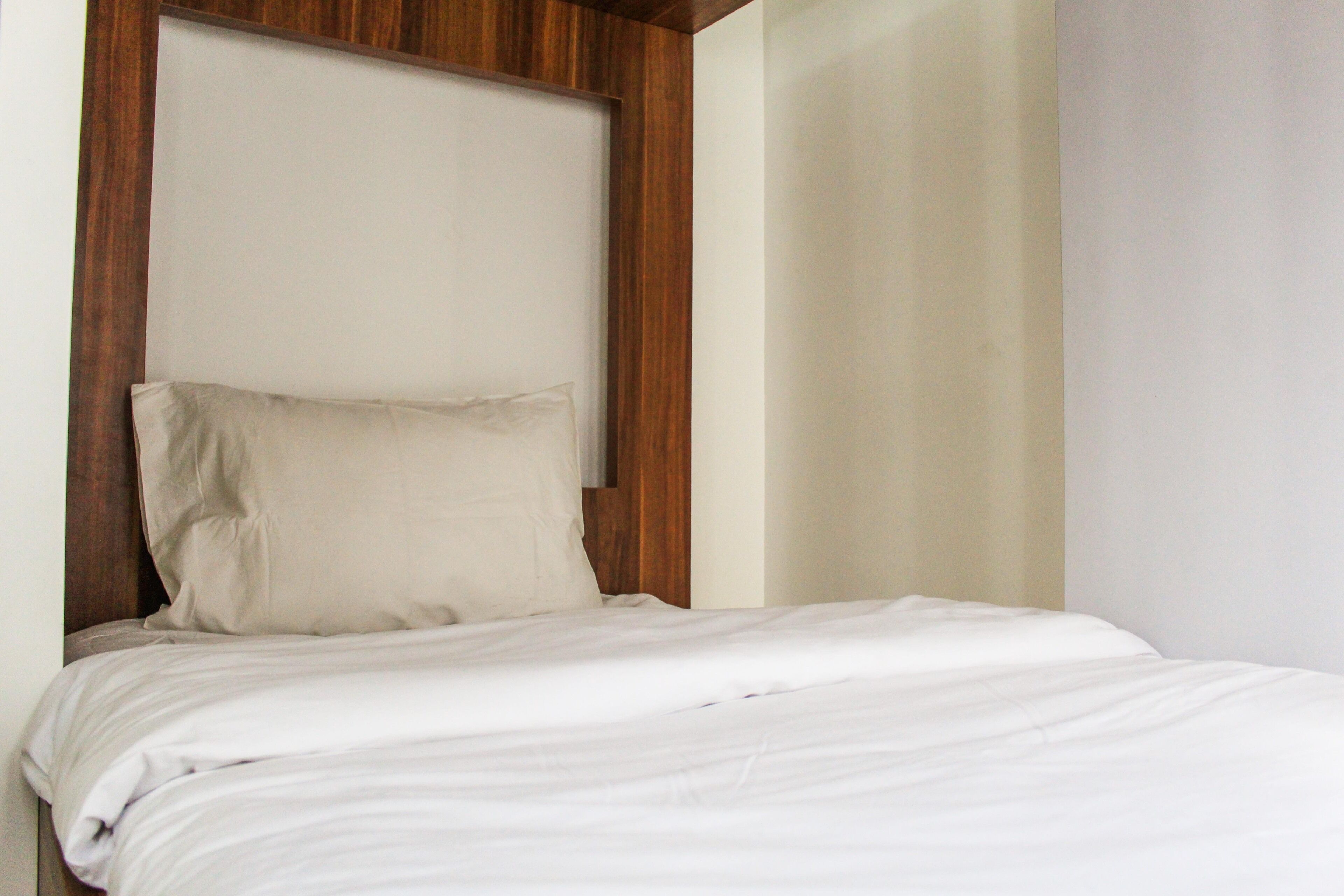 A bed with white bedding and a wooden headboard in a room with plain walls.