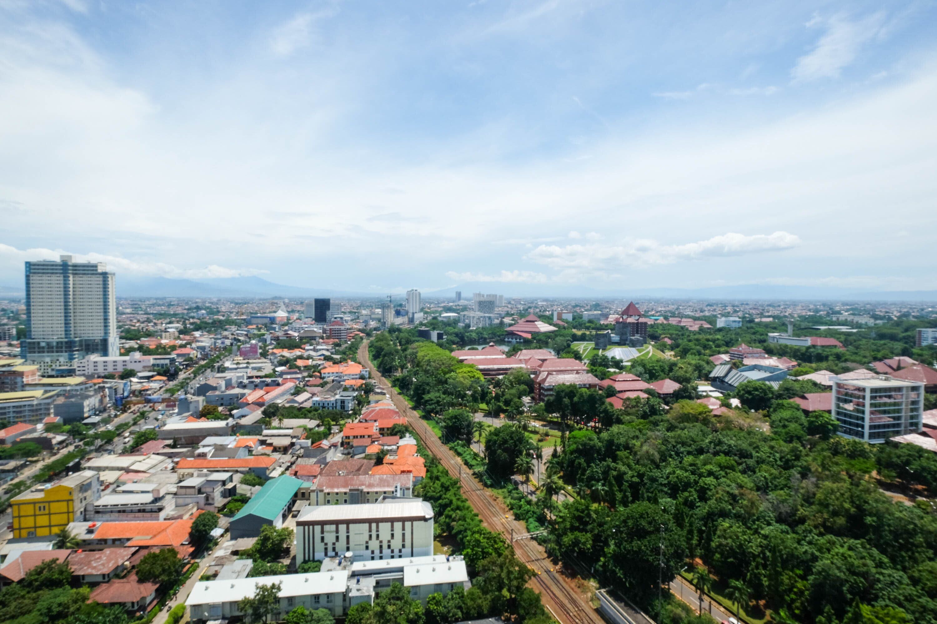 A cityscape with a mix of residential and commercial buildings, a prominent train track, and a distant mountain range.