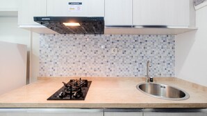 A kitchen with a gas stove, a stainless steel sink, and a tiled backsplash. - Cozy and Modern 1BR Apartment at Atlanta Residences By Travelio (Depok)
