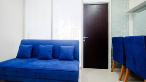 A room with a blue sofa, a dark door, and a table with blue chairs. - Cozy and Modern 1BR Apartment at Atlanta Residences By Travelio (Depok)