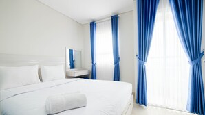 A hotel room with a large bed, white bedding, a nightstand with a mirror, and blue curtains. - Cozy and Modern 1BR Apartment at Atlanta Residences By Travelio (Depok)