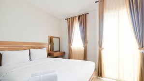 A hotel room with a large bed, a wooden headboard, a nightstand, a mirror, and curtains on the windows. - Warm and Homey 1BR Apartment at Atlanta Residences By Travelio (Depok)