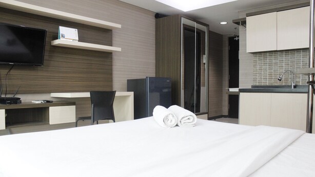 A hotel room with a bed, a desk, a chair, a television, and a kitchenette. - Prime & Comfy Studio @ Tamansari La Grande Apartment By Travelio (Bandung)