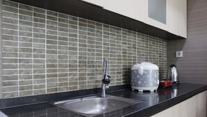 A kitchen with a black countertop, a stainless steel sink, and a tiled backsplash. - Prime & Comfy Studio @ Tamansari La Grande Apartment By Travelio (Bandung)