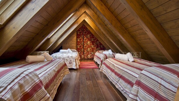 A cozy attic bedroom with two beds, wooden beams, and a floral curtain. - Sendrosa - Val de Ruda (Baqueira)