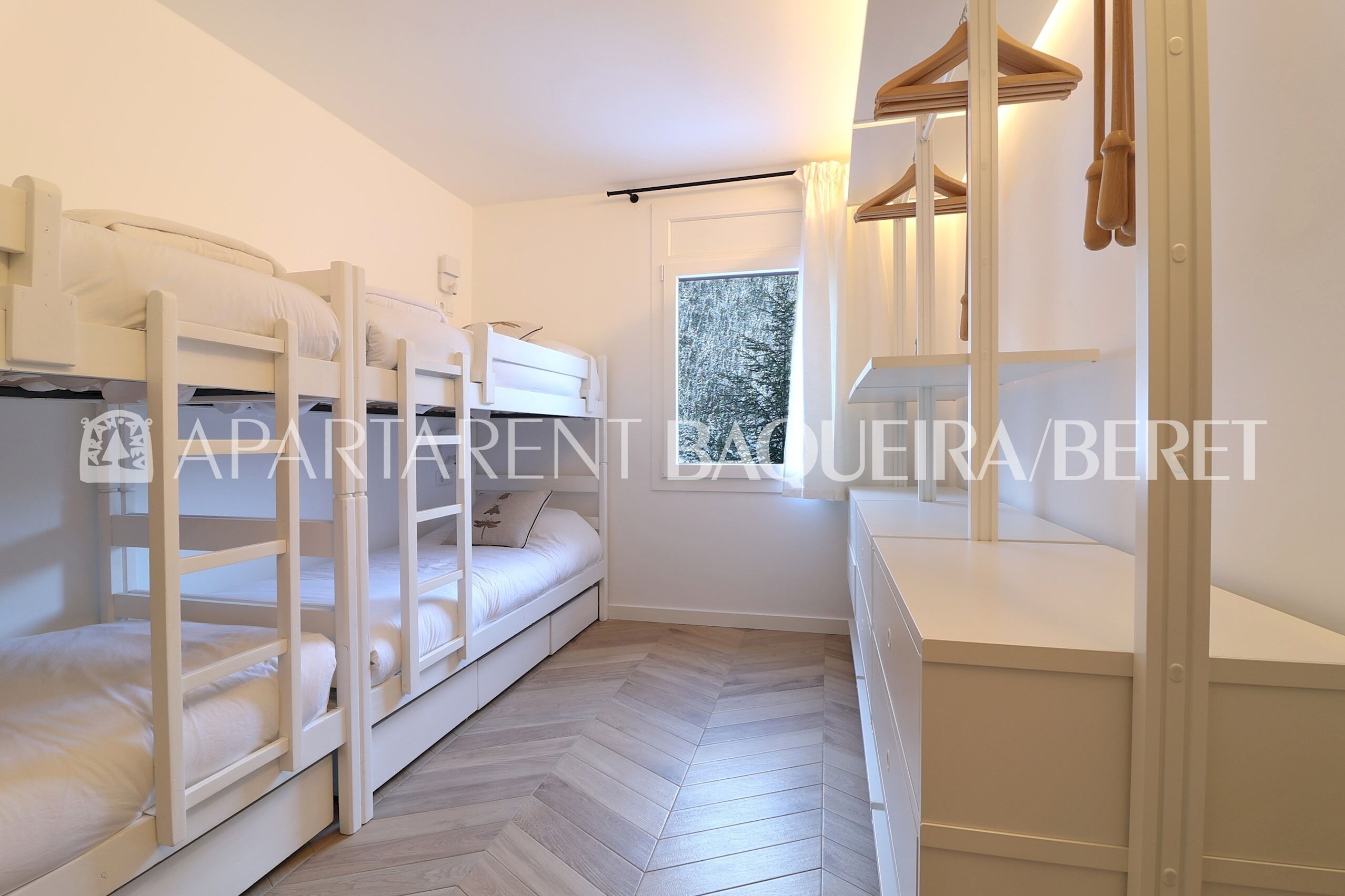 Une chambre avec des lits superposés, une fenêtre donnant sur les arbres et une table de chevet avec une lampe.
