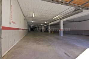Eine Innenparkgarage mit Betonböden und weißen Wänden, mit einem roten Streifen nahe der Decke und einem Schild an der linken Wand.