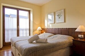 A double bed with a blanket and two pillows, a nightstand with a lamp, and a window with curtains.