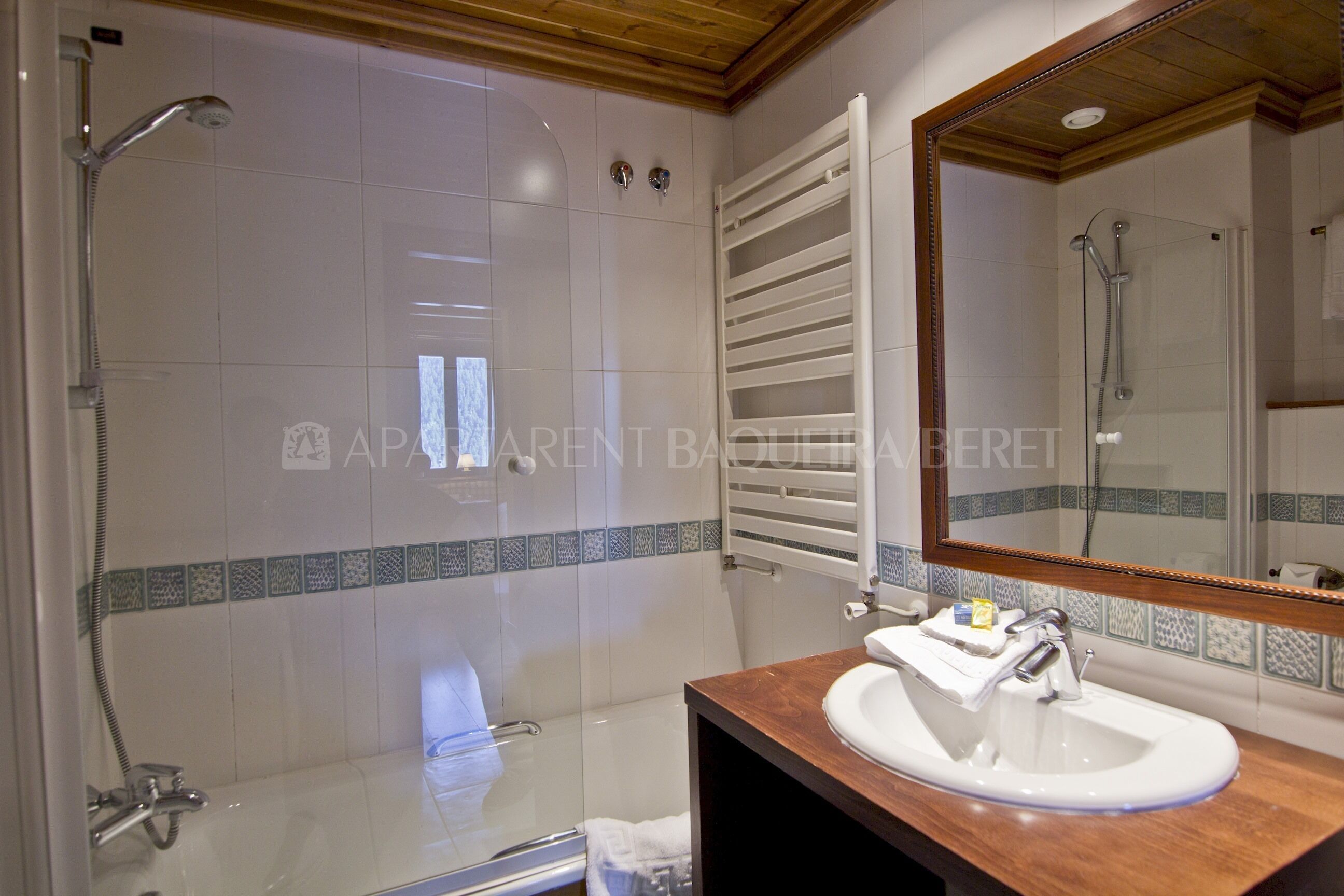 A bathroom with a glass-enclosed shower, a white sink, and a wooden vanity.