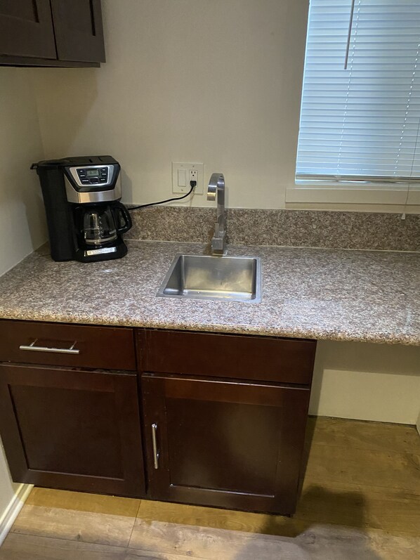 Kitchen area with granite countertop, stainless steel sink, coffee maker, and dark cabinets.