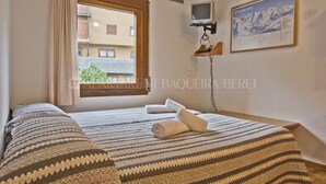 Habitación de hotel con cama, televisor montado en la pared y ventana con vistas a edificios.