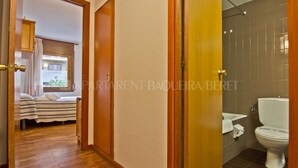 Habitación de hotel con piso de madera, una cama con manta a rayas y un baño con inodoro blanco y paredes de azulejos.