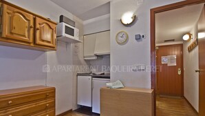 Una cocina compacta con armarios de madera, un microondas, un reloj y un refrigerador pequeño.