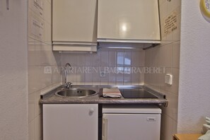 Una cocina compacta con armarios blancos, un lavamanos de acero inoxidable y un lavavajillas integrado.