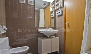 A bathroom with a sink, toilet, and bidet. There is a mirror above the sink and a wooden door to the right.