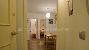 A hallway with a wooden floor, a dining table with chairs, and a hanging light fixture. - Urogallo - Edificio Aneto (Baqueira)