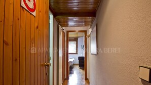 A narrow hallway with wooden walls and a tiled floor, leading to a bedroom with a bed and a nightstand.