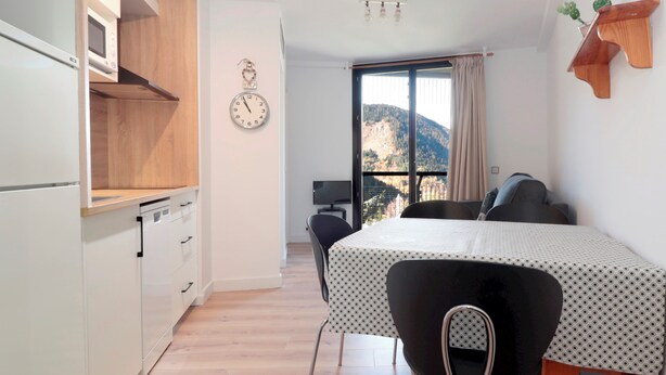 Une chambre à coucher de taille modeste, comprenant un lit, un petit bureau, une chaise, une horloge et une fenêtre donnant sur une vue sur la montagne.