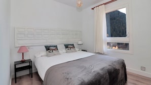 Une chambre à coucher comprenant un lit, une table de chevet, une lampe, une fenêtre donnant sur une forêt et un luminaire au plafond.