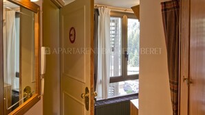 An open door leading to a room with a radiator, a window with curtains, and a view of the outside. - Garona - Edificio Aneto (Baqueira)