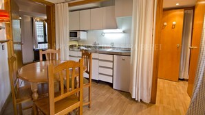 A compact kitchen with white cabinets, a microwave, and a sink. There is a wooden dining table with chairs. - Garona - Edificio Aneto (Baqueira)