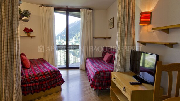 A bedroom with two beds, a TV, and a balcony with a mountain view. - Garona - Edificio Aneto (Baqueira)