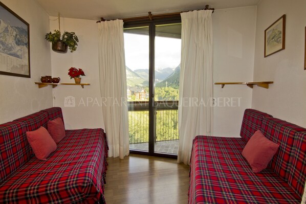 Ein Zimmer mit zwei betten in Karomuster, einem Fenster mit Bergblick und einer Pflanze, die von der Decke hängt.