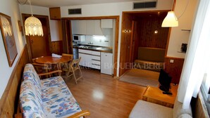 A compact living space with a sofa, a dining table, and a kitchenette. - Craba - Edificio Aneto (Baqueira)
