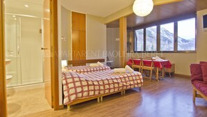 Une chambre avec deux lits, un coin repas comprenant une table et des chaises, et une grande fenêtre donnant sur la montagne.
