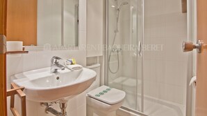 Un baño con lavamanos blanco, inodoro y ducha con mampara de vidrio.