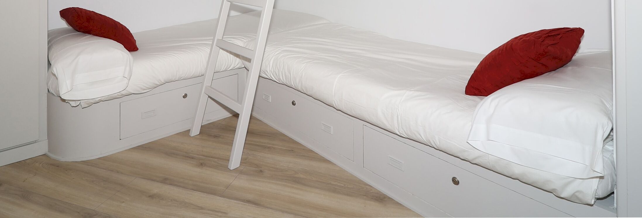 Una cama doble con escalera, ropa de cama blanca y almohadas rojas.