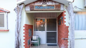 A building entrance with a sign reading "Robinson" and a green chair outside. - Minshuku Robinson (Zamami)