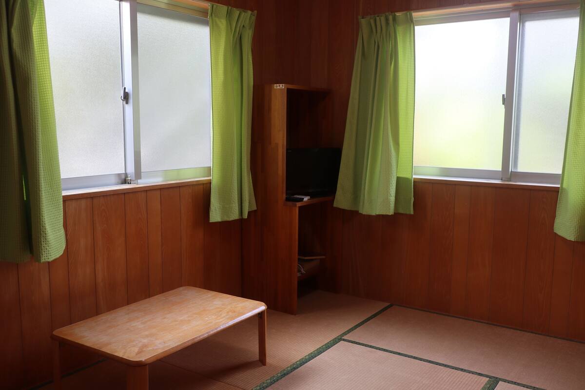 A room with wooden walls, a tatami mat floor, a wooden bench, and a television on a shelf.