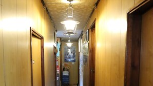 A narrow hallway with wooden walls and a wooden floor. There are doors on both sides and a ceiling light fixture. - Minshuku Robinson (Zamami)