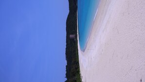 A beach with clear blue water, white sand, and a small building on the left. - Minshuku Robinson (Zamami)