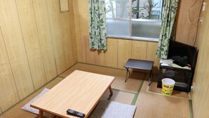 A small room with a wooden floor, a tatami mat, a wooden table, a small bench, a television, and a bucket. - Minshuku Robinson (Zamami)