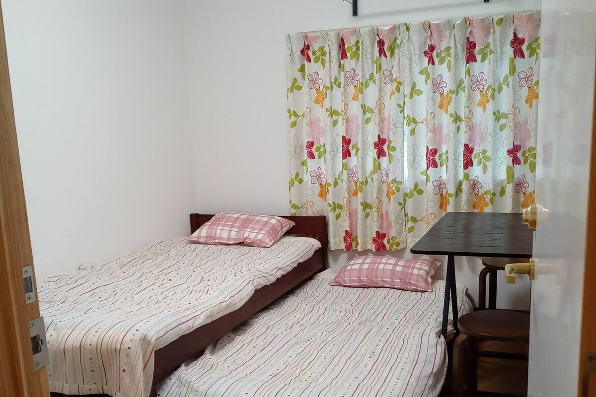 A room with two single beds, a small table, and a chair.