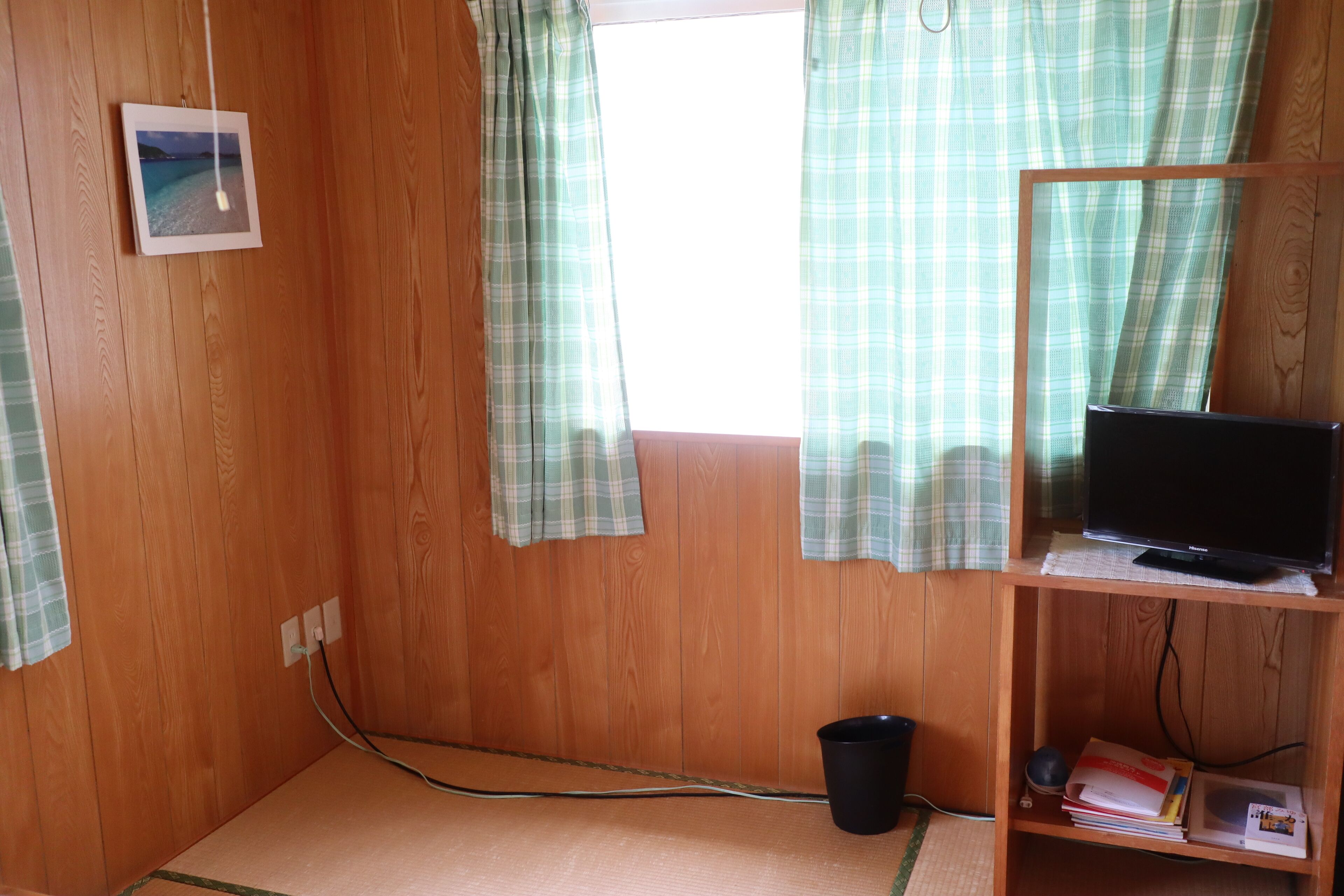 A room with wooden walls, a television on a wooden stand, a small black trash bin, and a power outlet on the wall.