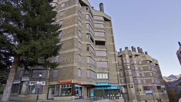 Un edificio de varios pisos con comercios en la planta baja, incluyendo una panadería y una escuela.