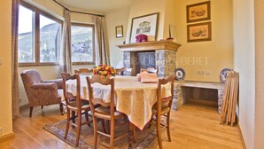 Un comedor con una mesa dispuesta para cuatro personas, rodeada de sillas de madera, una chimenea y cuadros en la pared.