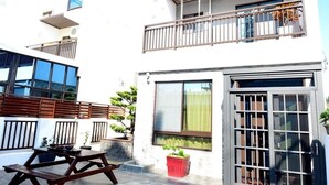 A modern two-story building with a balcony, a dining area with a table and benches, and a potted plant. - Shui Yifang B&B (Magong)