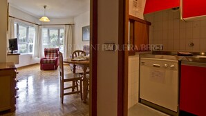 A room with a wooden dining table, chairs, a television, and a window with curtains.