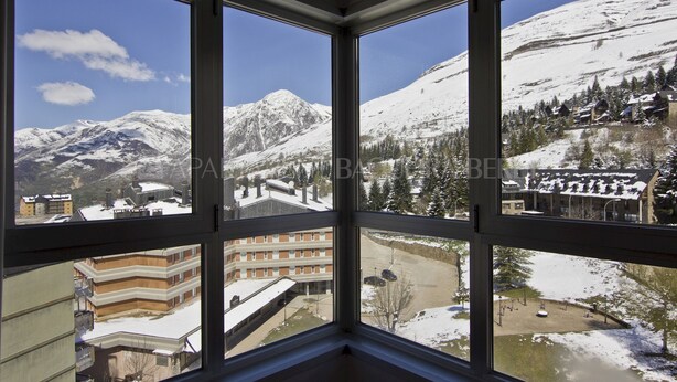 A corner room with large windows offering a view of snow-covered mountains and a ski resort.