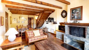 A cozy living room with a wooden staircase, a fireplace, and a dining area. - Cumbres - Nin de Beret (Baqueira)