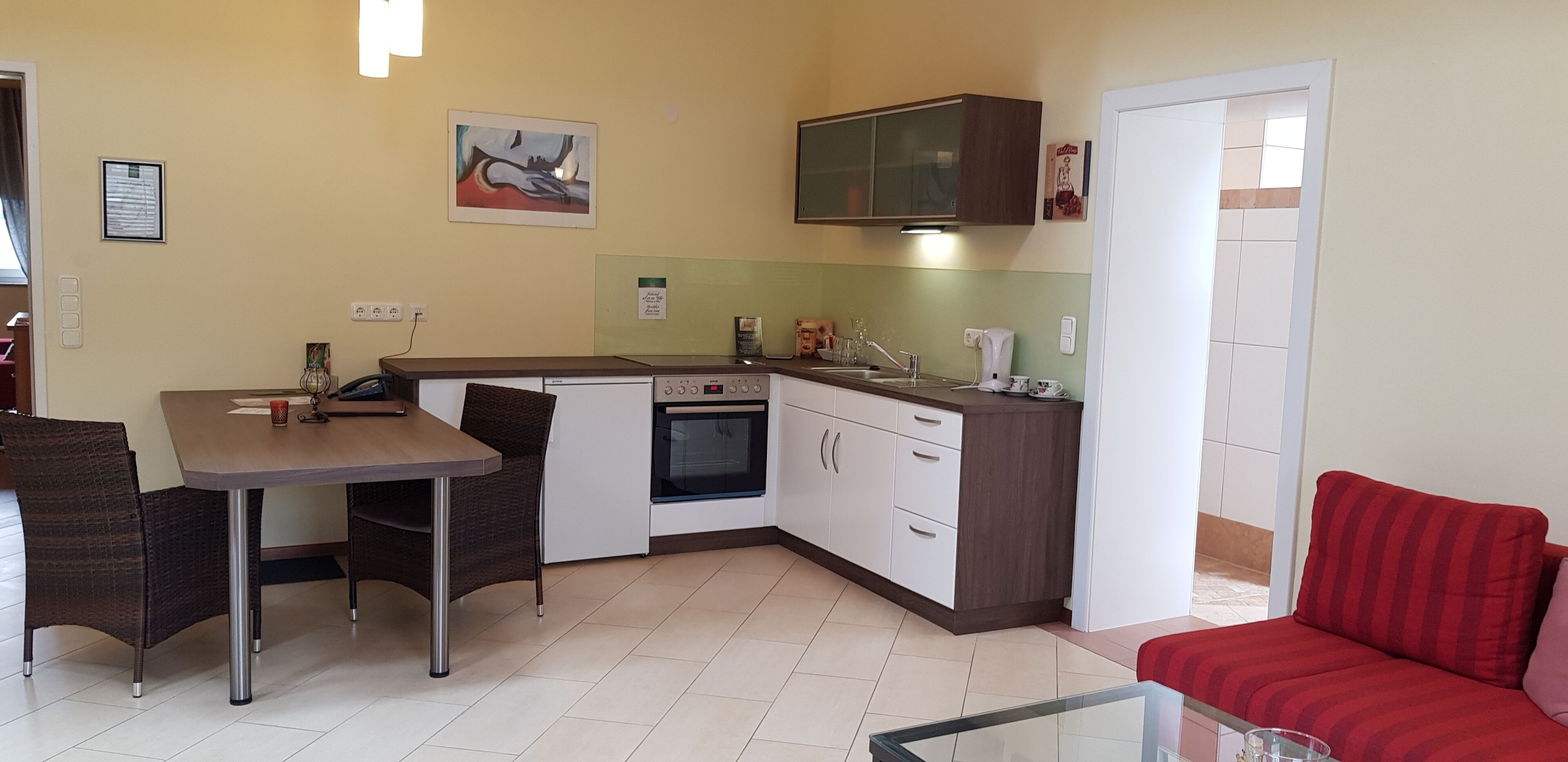 A compact kitchen with a dining area, a built-in oven, and a red sofa.