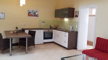 A compact kitchen with a dining area, a built-in oven, and a red sofa.