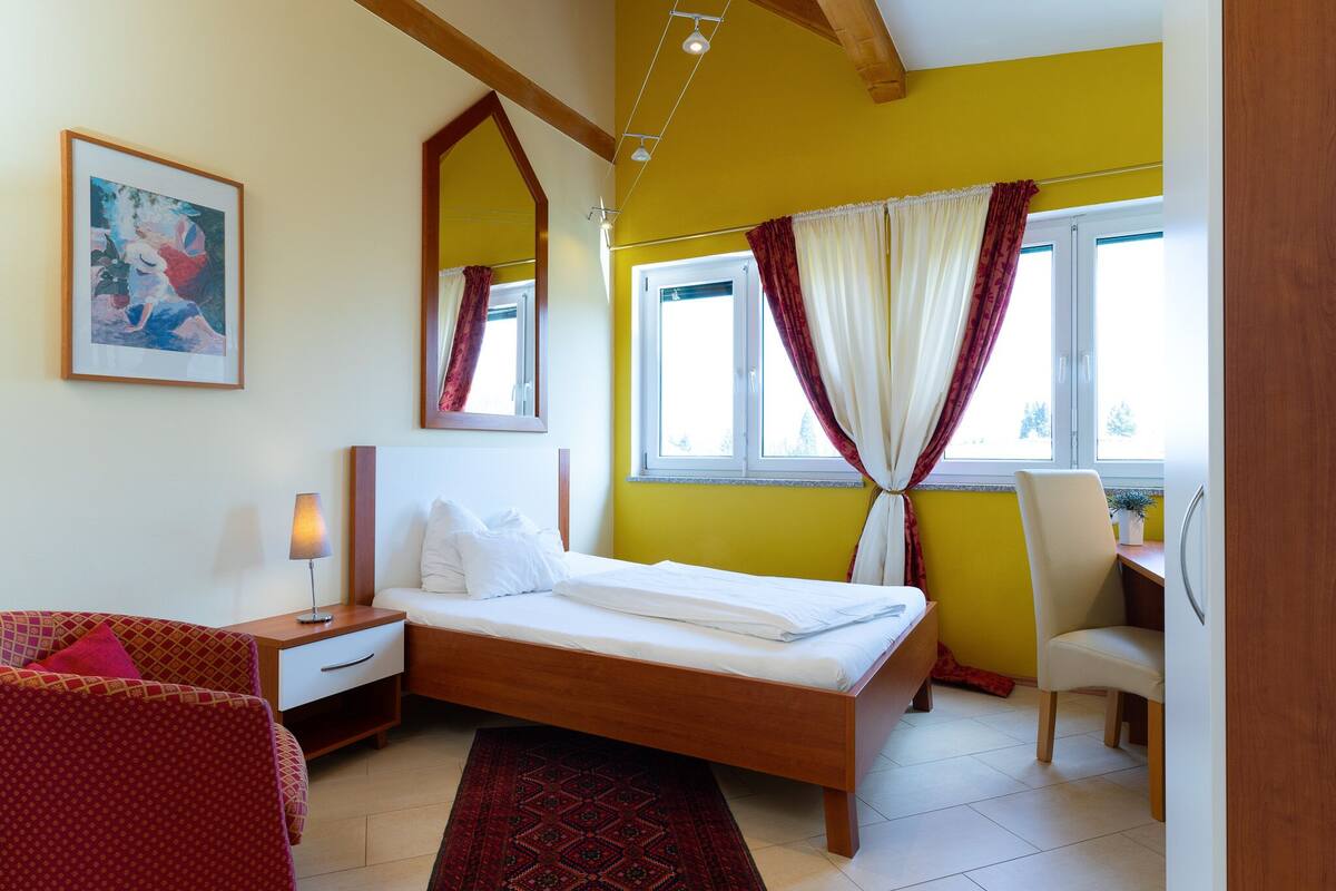 A bedroom with a bed, a desk, a chair, a lamp, and a window with curtains.