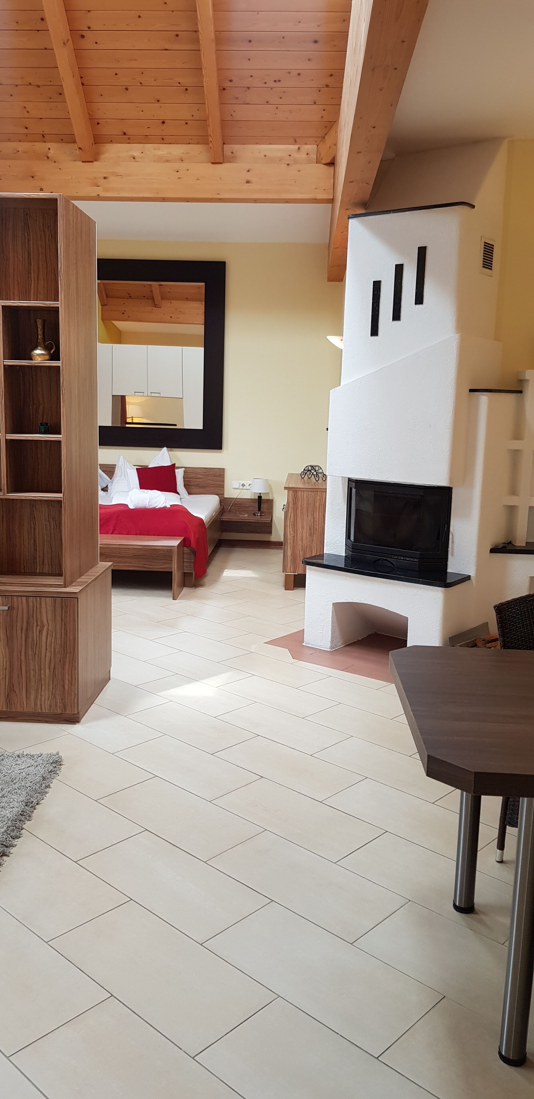 Ein modernes Wohnzimmer mit Kamin, einem Bett mit roter Bettwäsche und einem Holzregal.